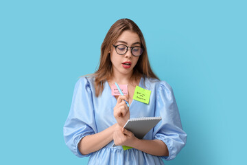 Wall Mural - Young woman with sticky notes, notebook and pen on blue background. Reminder concept