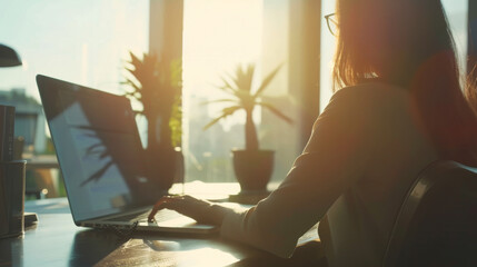 Sticker - Sunlight pours into a modern office as a person works on a laptop amidst green potted plants, creating a tranquil and productive environment.