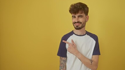 Wall Mural - Young, cheerful hispanic man with a natural happy expression on his face, standing aside, pointing and smiling up over an isolated yellow background.