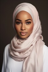 Wall Mural - Portrait of a woman wearing a beige hijab and white top against a dark background.