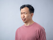 © Daniel - An Asian man in a pink shirt makes a skeptical and uncomfortable expression, as if reacting to something unpleasant. The plain light blue background highlights his displeased