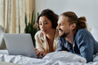 © LIGHTFIELD STUDIOS - A loving couple relaxing together on a bed, browsing a laptop.