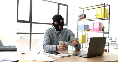 Internet scammer in balaclava with headphones with microphone counting money in front of laptop 4k movie. Cheating and theft online concept
