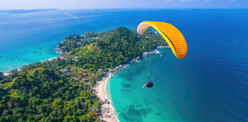 Wall Mural - A photo shows someone paragliding over the sea in Phuket, Thailand with lush greenery and sandy beaches on either sides. The person is wearing a yellow parachute, gliding above clear blue water agains