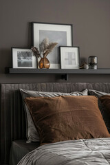 Wall Mural - A close-up photo of an elegant dark grey wall shelf with picture frames, in the background is a modern bed with a brown velvet headboard and striped cover. The walls have a dark gray color.