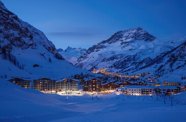 Wall Mural - A panoramic view of the snow-covered town of val d'isere at night, surrounded by majestic mountains and illuminated buildings.