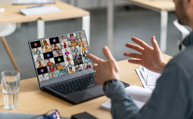 Aufkleber - A man sits at a desk in front of a laptop. He is gesturing with his hands and looking at the screen, which displays a grid of video calls with multiple people.