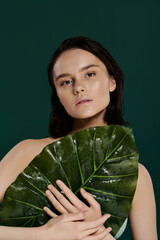 Wall Mural - A woman poses with a large leaf against a vibrant green backdrop.