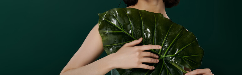 A woman poses with a large, wet leaf against a dark green backdrop.