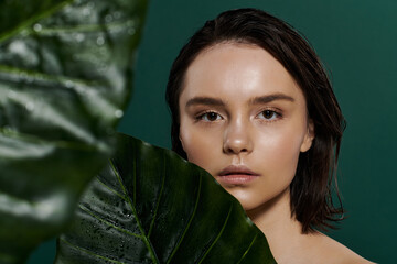 Wall Mural - A woman poses with a leafy green plant in front of a vibrant backdrop.