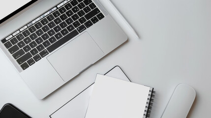 A white notebook sits open next to a Macbook Pro. The Macbook Pro has a blank white screen. The devices are on a white background in Batumi, Georgia. (April 10, 2023)