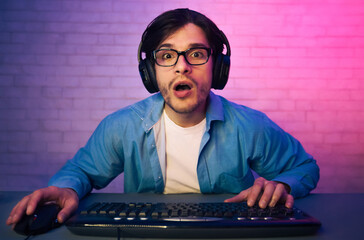 Leinwandbilder - a young man wearing headphones and glasses sits in front of a keyboard and mouse, looking surprised 