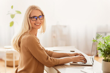Poster - A woman with blonde hair and glasses smiles while working on a laptop at her desk.