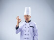 © Daniel - A cheerful Asian male chef in a white uniform and hat makes an 'OK' hand gesture thumb, expressing satisfaction and positivity against a light blue background. The setting is professional and engaging