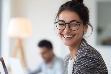 Poster - Businesswoman lawyer in stylish attire and glasses joyfully working on laptop indoors with white background, man and lamp blurred in foreground.