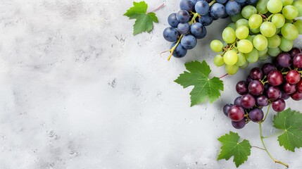 A variety of grape clusters, including green, red, and pink grapes, are arranged on a light pink surface, with some green leaves