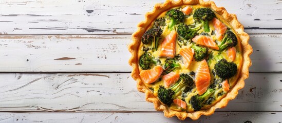 Poster - Top-down view of a quiche tart containing smoked salmon, broccoli, and spinach on a white wooden background, designed for a copy space image.