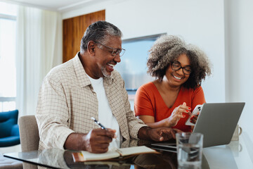 Happy senior couple budgeting at home using laptop and smartphone