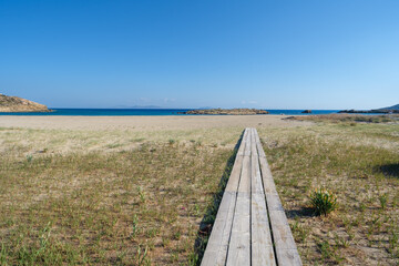 view of a wooden path leading to the b eautiful sandy beach of magganari in ios greece