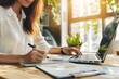 © SSTC AI Photo&Video - Woman wearing glasses and writing at a desk with a laptop, highlighting concentration and productivity in a bright workspace..