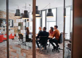 In a sleek glass office space, a team of business professionals engage in lively discussions and exchange strategic ideas, showcasing collaboration and innovation at the heart of modern corporate