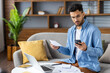 © Tetiana - Worried young Indian man working from home on laptop, seriously checking and holding documents and mobile phone