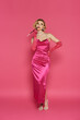 © LIGHTFIELD STUDIOS - A woman in a pink satin dress stands against a pink backdrop, holding a cigarette holder.