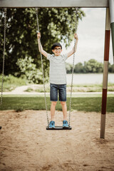 Joyful Young Teen Boy Standing on a Swing at Playground, Looking to the Right Side While Playing