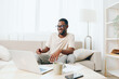 © SHOTPRIME STUDIO - Smiling African American Man Typing on Laptop while Working from Home on the Modern Sofa in the Living Room He is a Freelancer with a Millennial Lifestyle, enjoying the comfort of his apartment The