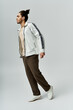 © LIGHTFIELD STUDIOS - A young African American man in a stylish white jacket and brown pants poses against a grey background.
