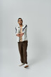 © LIGHTFIELD STUDIOS - A young African American man in a white jacket and brown pants poses against a grey background.