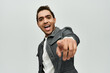 © LIGHTFIELD STUDIOS - A stylish African American man in a coat, smiles and points at the camera in a studio setting.