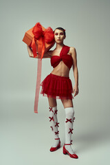 Wall Mural - A young woman in a red outfit and a bow holds a large gift box in a studio setting.