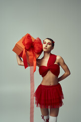 Wall Mural - A young woman in a red outfit with a bow holds a large gift box against her shoulder.