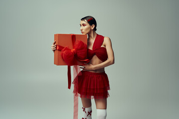 Wall Mural - A young woman in a red outfit holds a large gift box with a red bow in a studio setting.