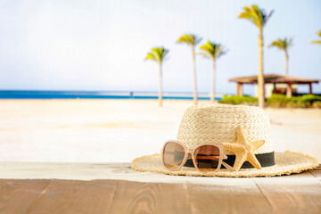 Wall Mural - Straw hat and sunglasses on a tropical beach with palm trees and sea background.