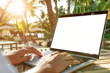A person typing on a laptop computer with a mock up blank white screen and a cafe in a tropical luxury resort in the background