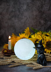 Sticker - black cat figurine, moon lamp, wheat ears and sunflowers on table,dark background. esoteric spiritual ritual, witchcraft. symbol of harvest, Mabon holiday. moon esbat, autumnal equinox