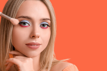 Sticker - Beautiful young woman with brush applying colorful eyeshadows on orange background