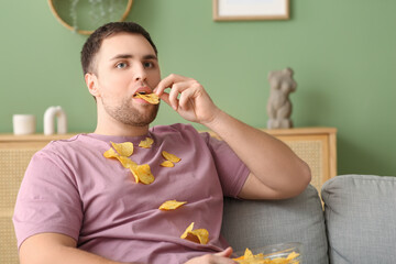 Sticker - Handsome young man with scattered tasty potato chips at home