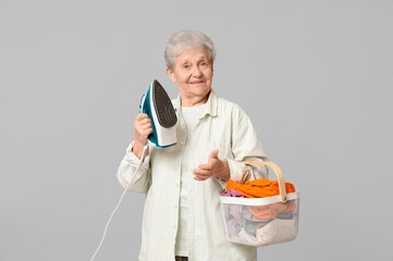 Wall Mural - Happy senior woman with iron and basket of laundry on grey background