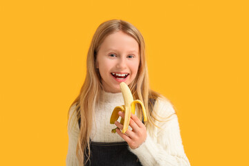 Canvas Print - Cute little girl eating ripe banana on orange background