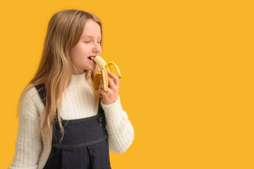 Wall Mural - Cute little girl eating ripe banana on orange background