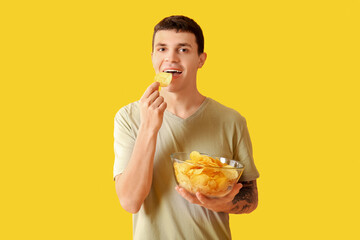 Wall Mural - Young man eating tasty potato chips on yellow background