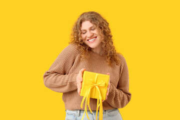 Sticker - Happy beautiful young woman with gift box on yellow background