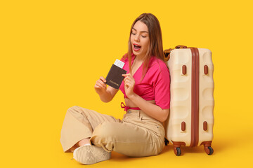 Wall Mural - Shocked young woman with passport and suitcase on yellow background