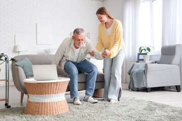 Poster - Female caregiver helping senior man to stand up from sofa in nursing home