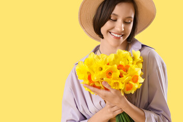 Wall Mural - Young woman in hat with daffodils on yellow background, closeup