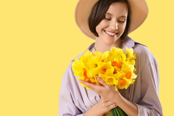 Canvas Print - Young woman in hat with daffodils on yellow background, closeup