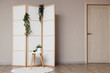 © Pixel-Shot - Folding screen with plants and table near light wall in room